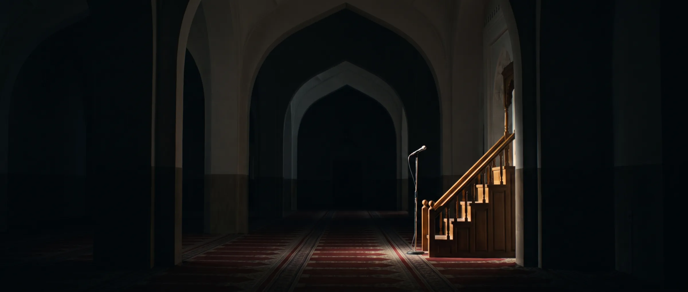An empty mosque hall at night, a single microphone lit beside the minbar